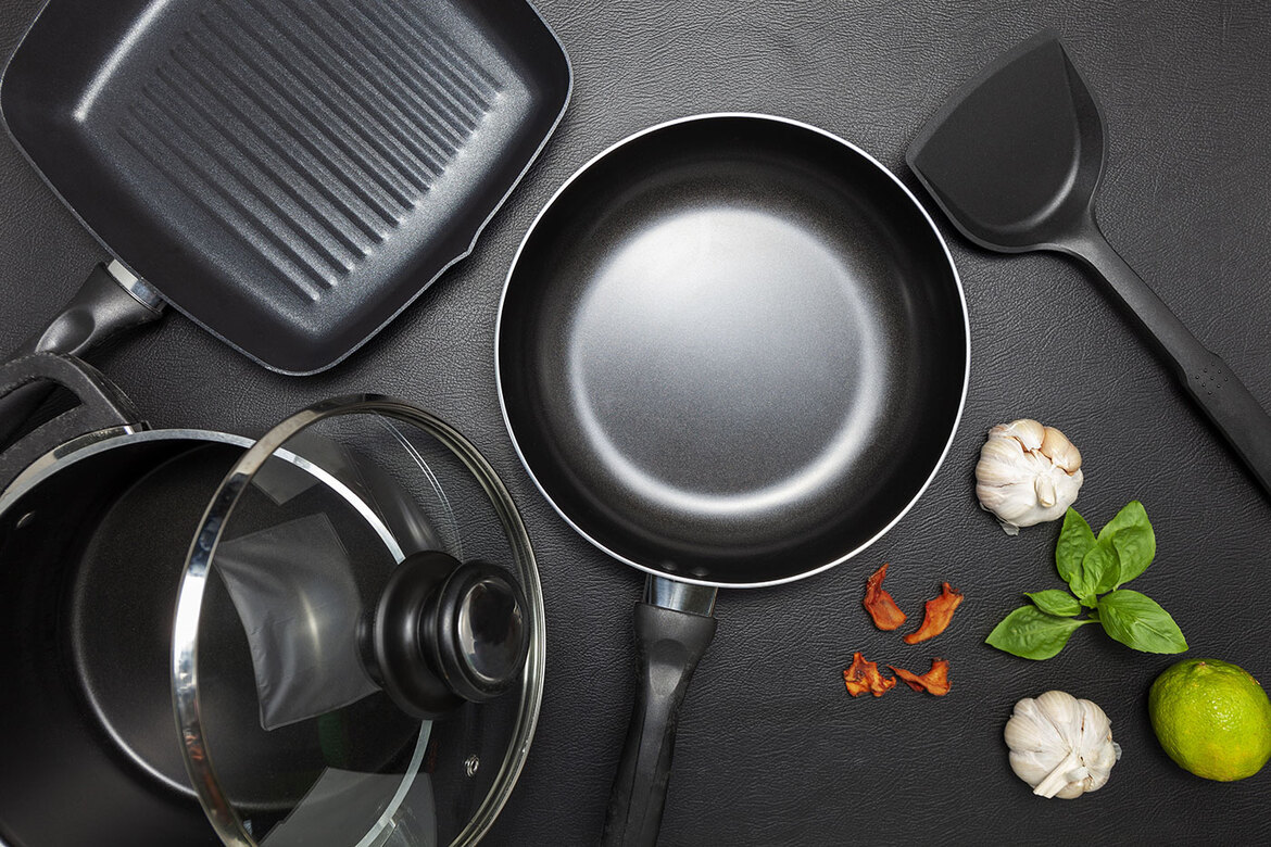 Alupfanne und -töpfe Pfanne aus Aluminium, Topf, Grillpfanne, Pfannenwender auf einem schwarzen Tisch von oben fotografiert