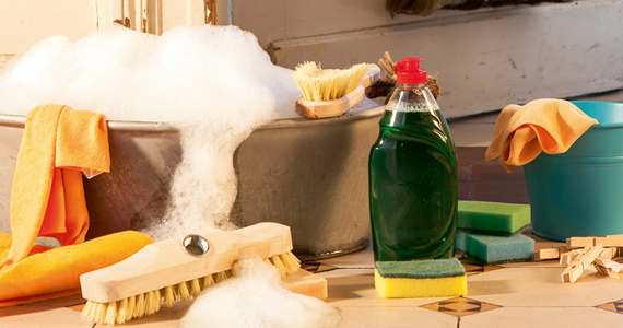 Prostředek na mytí nádobí, čisticí kartáče, hadry a houbičky vedle kbelíku